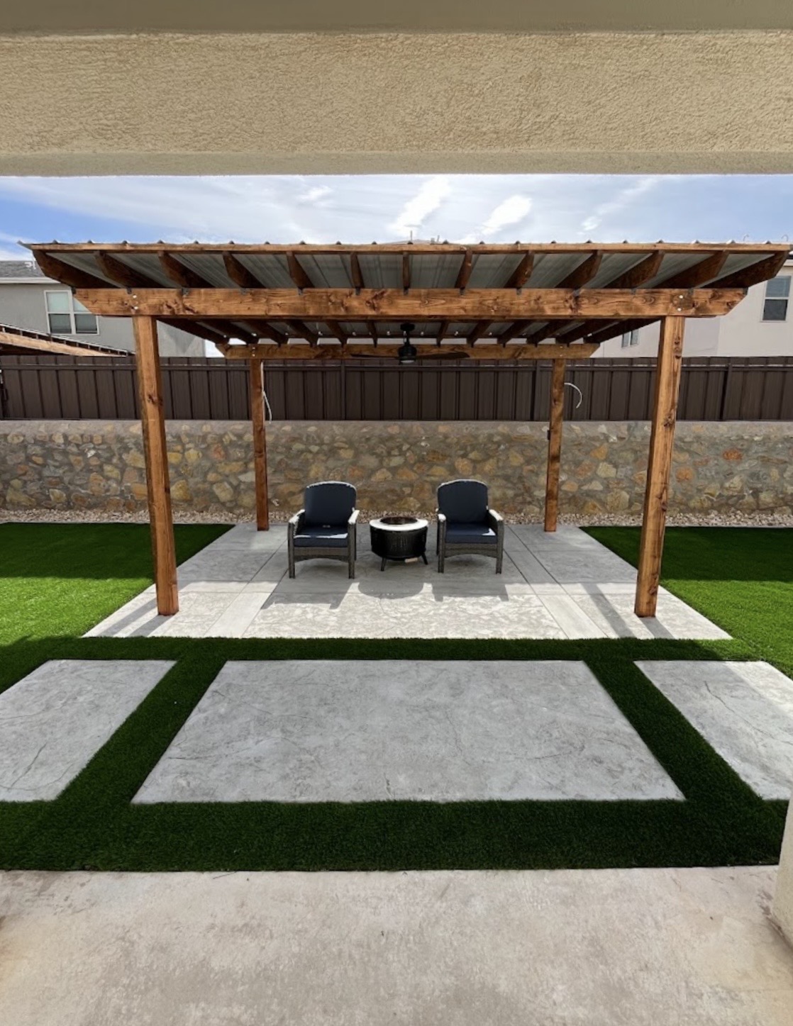 Wooden pergola over a stamped concrete patio with artificial turf and a stone wall in El Paso